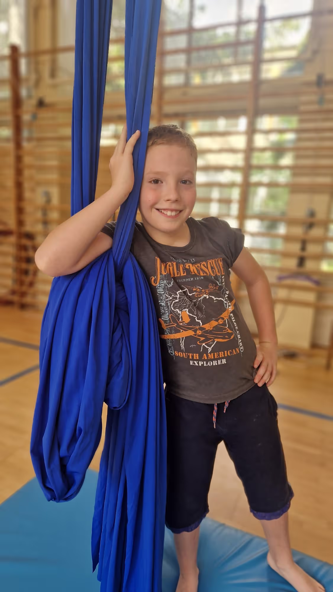 Uśmiechnięty chłopiec oparty o szarfę (aerial silk) na kolonii Akademii Everest.